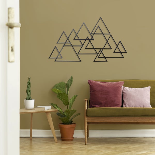Wanddekoration aus schwarzen Metalldreiecken in Berg-Optik über einem grünen Sofa in einem hellen, modern eingerichteten Wohnzimmer.