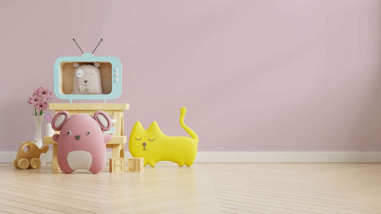 Ein helles Kinderzimmer mit einer zartrosa Wand, einer weißen Fußleiste und hellem Holzboden. Dekorative Holzmöbel und bunte Stofftiere.