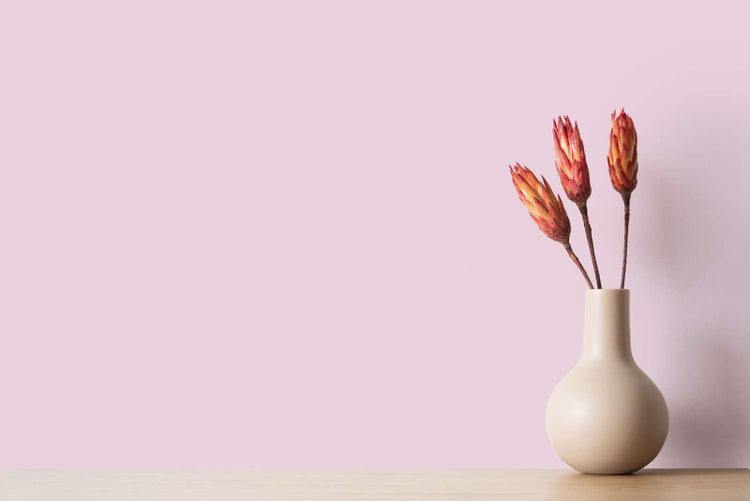 Minimalistische Dekoration bestehend aus einer runden beigen Keramikvase mit drei getrockneten roten Blumen auf einer hellen Holzoberfläche.