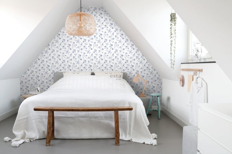 Helles Schlafzimmer mit Bett vor blauer Blumentapete