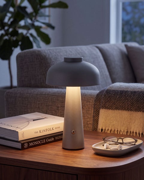 Moderne Pilz Tischlampe mit Diffusor auf einem Holztisch neben Büchern und einer Ablageschale in einem gemütlichen Wohnbereich.