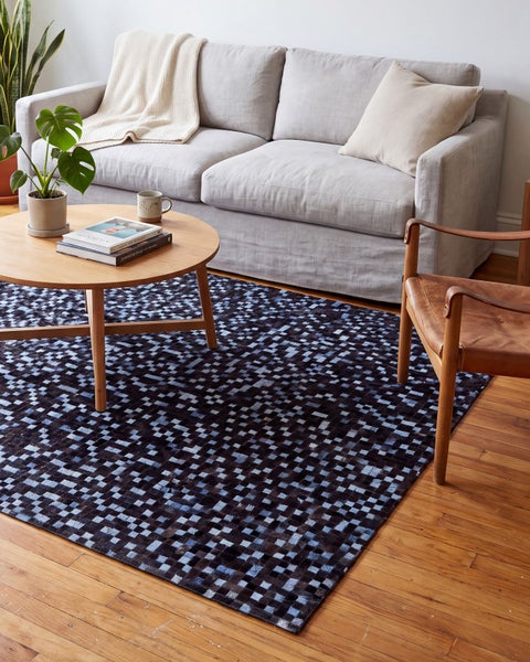 Wohnzimmer mit einem rechteckigen Teppich aus Fell im Schachbrettmuster, platziert vor einem Sofa auf einem Holzboden mit Holztisch und Stuhl.