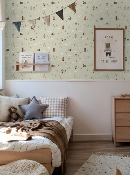 Kinderzimmer mit einer Vliestapete mit Wald- und Hausmotiven, einem Holzbett mit Kissen, einer Kommode und Wanddekoration.
