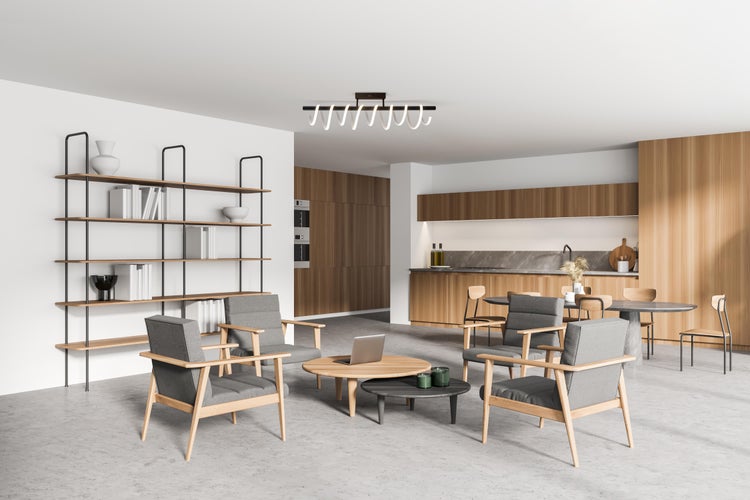 Helles Wohnzimmer mit Regalen, grauen Sesseln, Couchtischen und einer Küchenzeile mit Essbereich