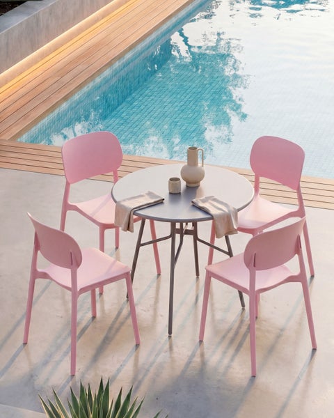 Modernes Gartenmöbel-Set mit vier rosa Stühlen und einem runden grauen Tisch an einem Pool auf einer Terrasse mit Holzdeck.