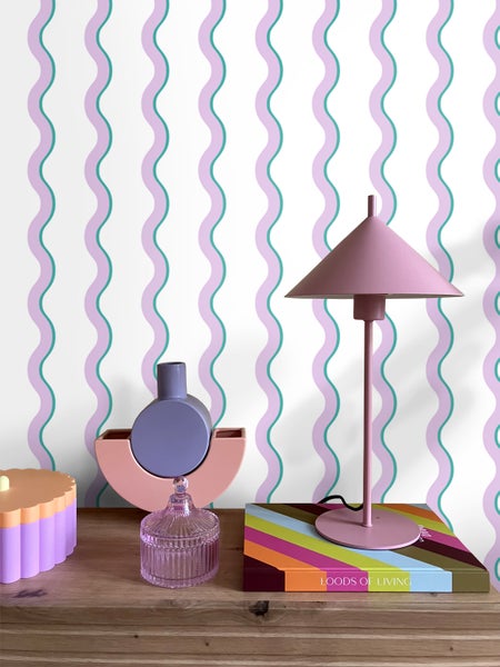 Dekorative Szene mit Lampe, Vase und Dose auf einem Tisch vor einer gemusterten Tapete.