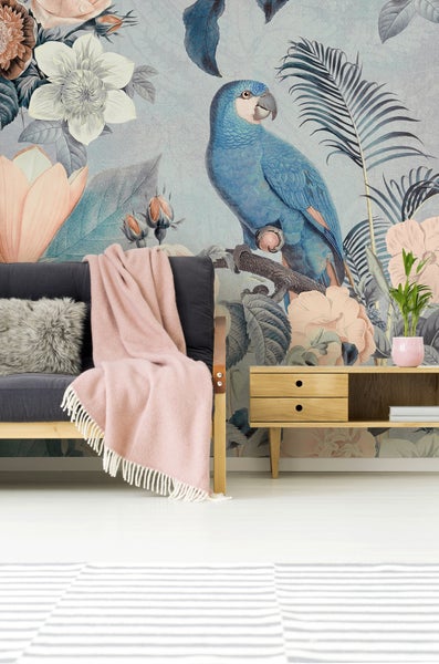 Hell gestaltetes Wohnzimmer mit botanischer Fototapete mit Papagei und Blumen hinter einem dunklen Sofa mit Decke und einem Sideboard aus Holz.