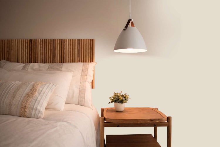 Schlafzimmer mit Kopfteil aus Holzlamellen, weißem Bettzeug, Nachttisch aus Holz und einer Glocken-Pendelleuchte.