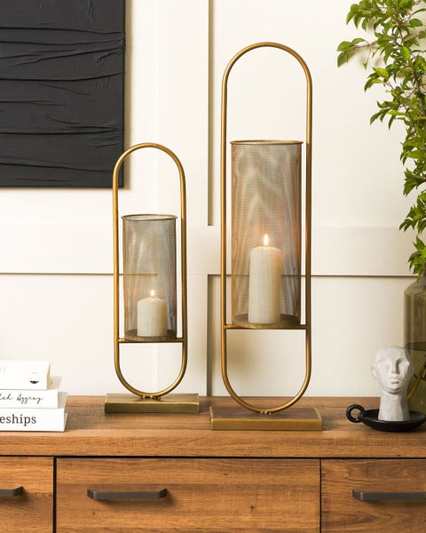 Zwei goldfarbene Kerzenständer mit Kerzen auf einem Holzschrank