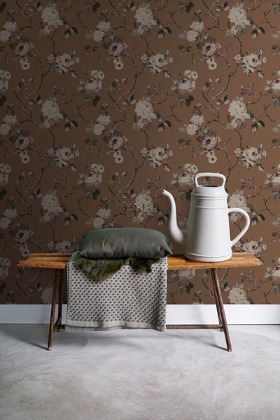 Szene mit einer braunen Tapete mit Blumenmuster, einer Bank, einem Kissen und einer weißen Gießkanne.