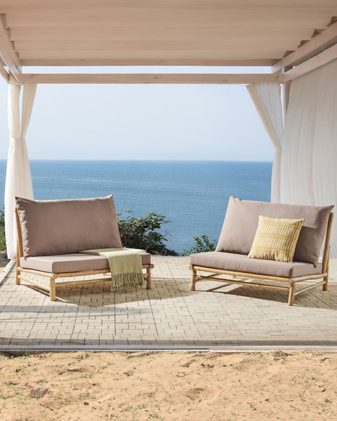 Zwei Bambussessel mit Kissen und Decke unter einem Pavillon mit Meerblick.