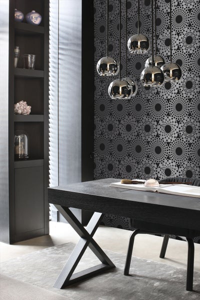 Innenraum mit schwarzem Schreibtisch, Regalen und Kugelpendelleuchten vor gemusterter Tapete.