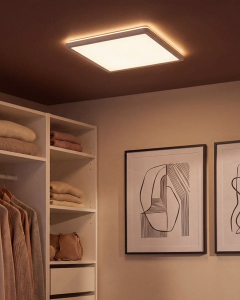 Quadratische LED Deckenleuchte montiert in einem modern eingerichteten begehbaren Kleiderschrank mit Kleiderregalen und Wandbildern.