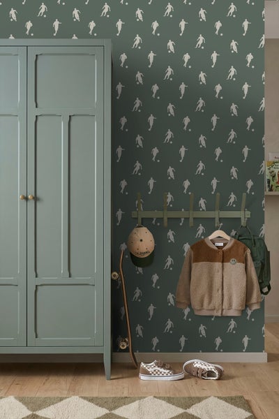 Kinderzimmer mit Fußballtapete in Dunkelgrün, grünem Kleiderschrank, Garderobe, Skateboard und Schuhen auf Holzboden.