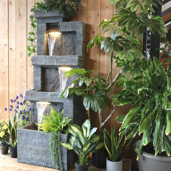 Mehrstufiger Zimmerbrunnen aus Stein mit Pflanzenarrangements