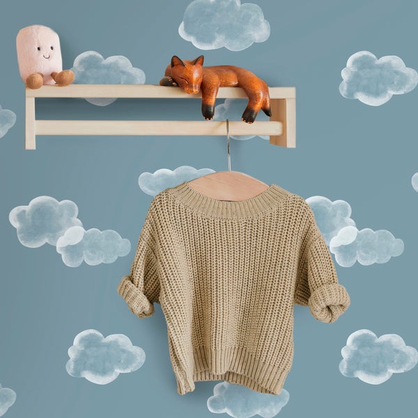 Kinderzimmertapete mit Wolkenmuster, Wandgestaltung mit Holzregal und aufgehängtem Strickpullover.