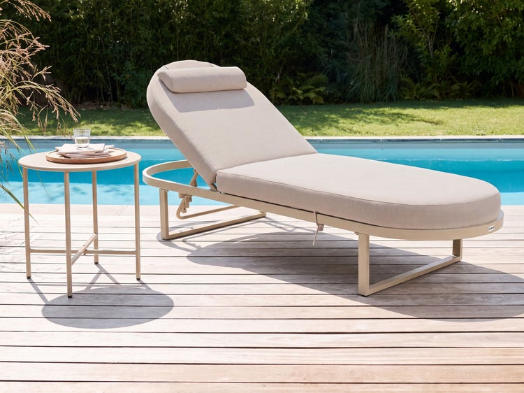 Sonnenliege mit Liegepolster und Kopfkissen neben einem runden Beistelltisch auf einer Holzterrasse am Pool im Garten
