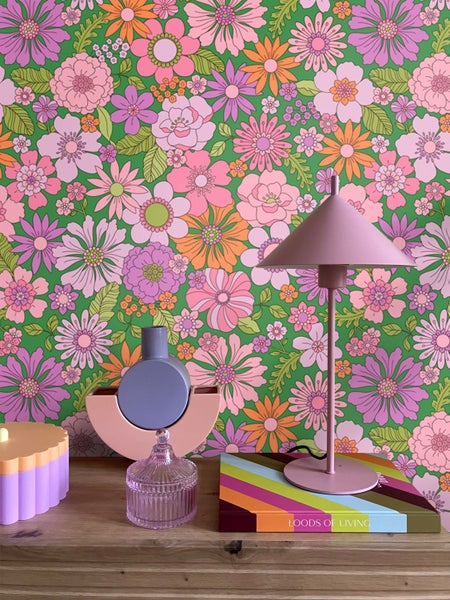 Dekorative Szene mit Lampe, Blumenvase und Wohnaccessoires vor einer floralen Tapete