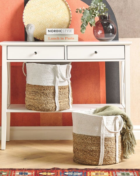Geflochtene Aufbewahrungskörbe aus Jute und weißem Seil in einem Wohnraum, einer auf einer Konsole und einer mit einer Decke auf dem Boden.