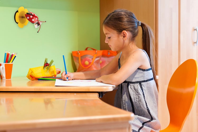 Mädchen sitzt an einem Schreibtisch und zeichnet, mit Schreibtischlampe und Stiften