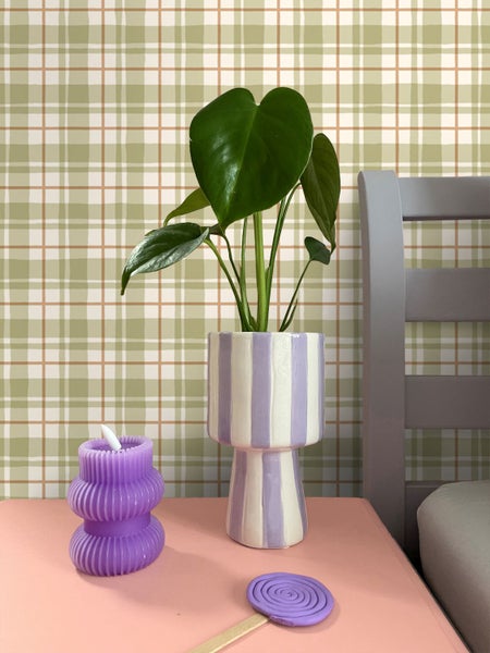 Dekorative Zimmerpflanze im gestreiften Topf neben Kerze auf einem Tisch