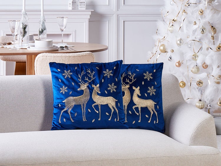 Dekorative Szene mit blauen Kissen mit Hirschmotiv auf einem Sofa, ergänzt durch einen Esstisch und einen Weihnachtsbaum.