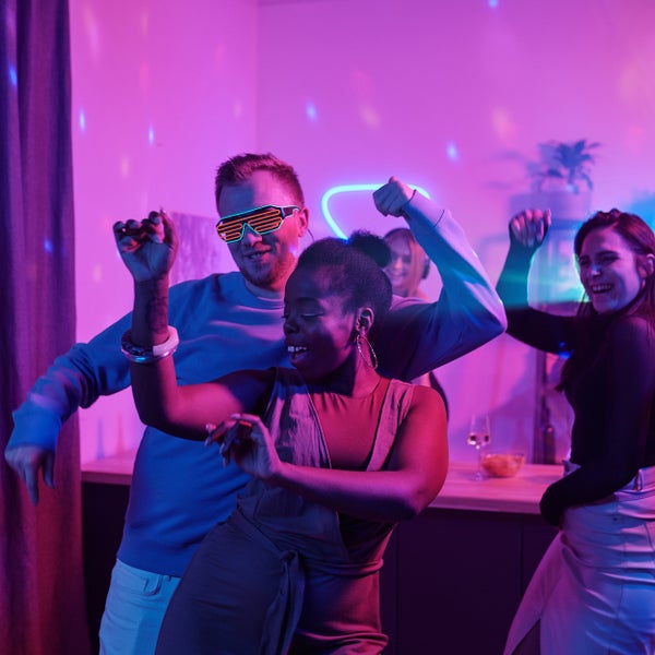 Eine Gruppe von Personen tanzt in einem Raum mit Neonbeleuchtung, was eine festliche Atmosphäre schafft.
