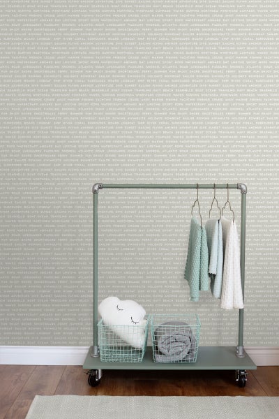 Dekorative Aufbewahrungslösung mit Kleiderständer, Körben und Textilien vor einer gemusterten Wand