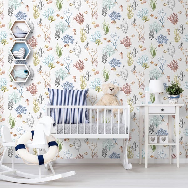 Helles, geordnetes Kinderzimmer mit maritimer Tapete mit Korallenmotiven, weißem Gitterbett aus Holz, Schaukelpferd und weißem Beistelltisch.