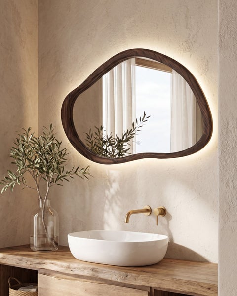 Modernes Badezimmer mit einem asymmetrischen Spiegel mit dunklem Holzrahmen und LED-Hintergrundbeleuchtung, Aufsatzwaschbecken und Wandarmatur.