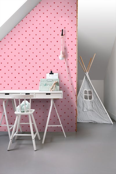 Kinderzimmer mit Schreibtisch, Stuhl und Spielzelt vor einer rosa Wandtapete mit Herzmuster