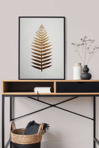 Moderner Innenraum mit gerahmtem Bild eines goldenen Farnblatts auf einem Konsolentisch aus Holz, Vasen und einem geflochtenen Korb.