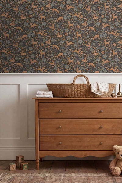 Tapete mit Reh und Blumenmuster in einem Kinderzimmer mit Holzkommode und geflochtenem Babykorb