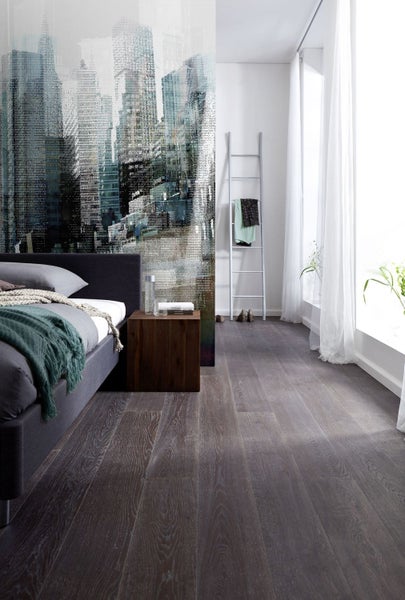 Schlafzimmer mit Bett, Holzboden und Wandbild mit Stadtmotiv.