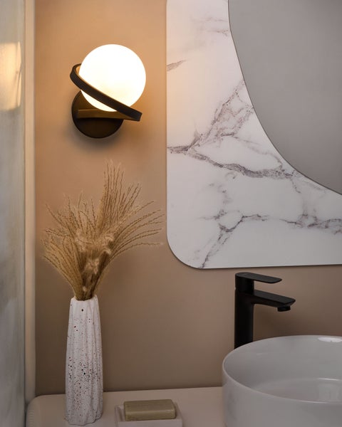 Badezimmeransicht mit Wandleuchte, Spiegel, Waschbecken und Armatur.