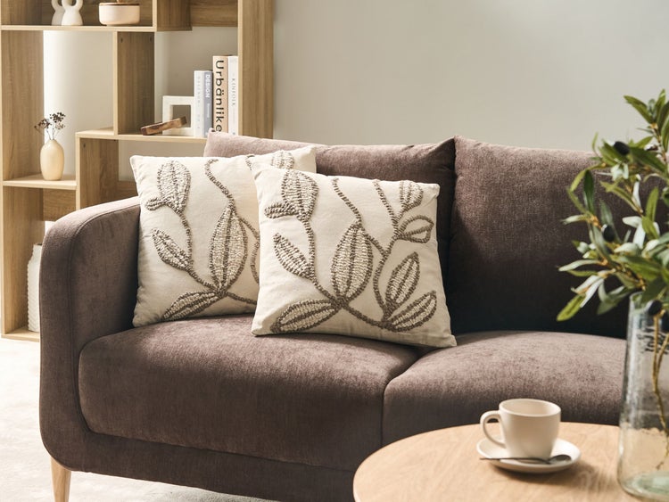 Wohnzimmer mit braunem Sofa und zwei Dekokissen mit Pflanzenmotiv