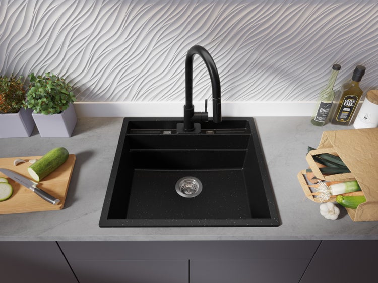 Schwarze Küchenspüle mit Armatur auf einer Küchentheke mit Gemüse und Ölflaschen.