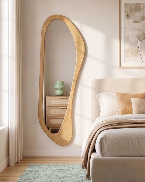 Ein organischer Ganzkörperspiegel mit Holzrahmen in einem modernen Schlafzimmer mit Bett und Kommode.