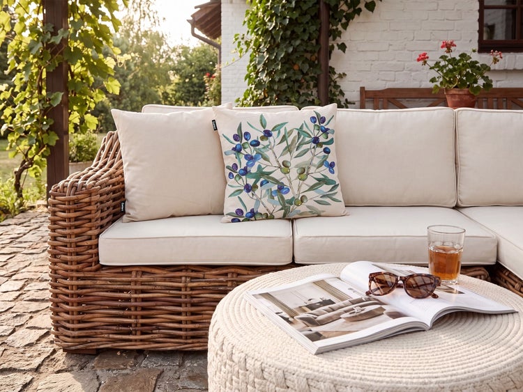 Rattan Gartensofa mit beigen Polstern und Zierkissen mit Olivenmotiv auf einer Terrasse.