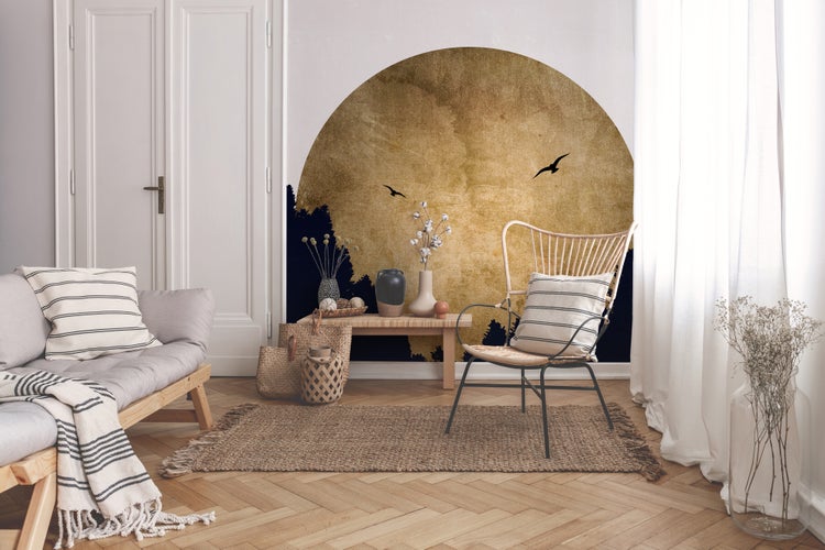 Helles Wohnzimmer mit kreisförmigem Wandtattoo einer Naturlandschaft. Einrichtung aus Holzsofa, Rattansessel, Jute-Teppich und Fischgrät-Parkett.