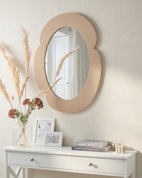 Wandspiegel mit wellenförmigem Rahmen über einem weißen Konsolentisch mit Vase und Dekoration in einem hellen Raum.