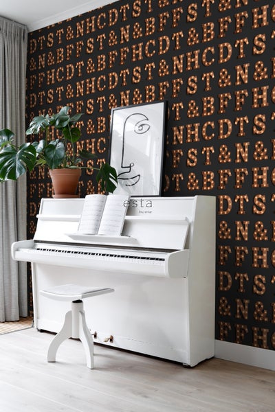 Szene mit einem weißen Klavier, einem Hocker, einer Zimmerpflanze und einer mit Buchstabenmustern verzierten Wand