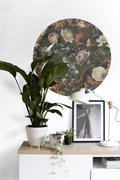 Dekorative Szene mit einer Zimmerpflanze, einer Lampe, einem Bilderrahmen und einer runden Wanddekoration mit Blumenmuster