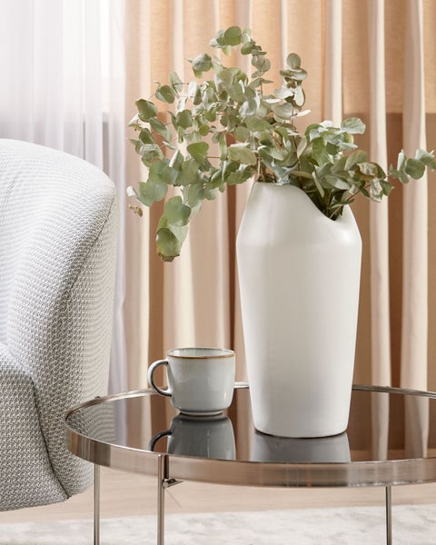 Dekoratives Arrangement mit Eukalyptus in Vase, Kaffeetasse und Beistelltisch im Wohnzimmer