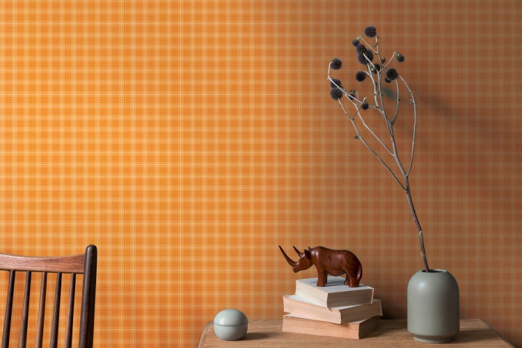 Dekoratives Stillleben mit gemusterter Tapete, Skulptur, Topfpflanze, Stift und Tasse auf einem Tisch