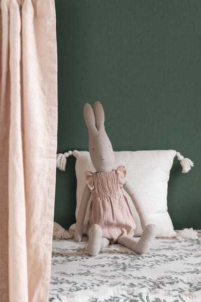 Dekoratives Stoffkaninchen sitzt auf einem Bett mit gemustertem Bezug und Kissen