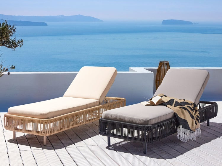 Zwei Liegestühle aus Rattan mit Polsterauflagen auf einer Terrasse mit Meerblick