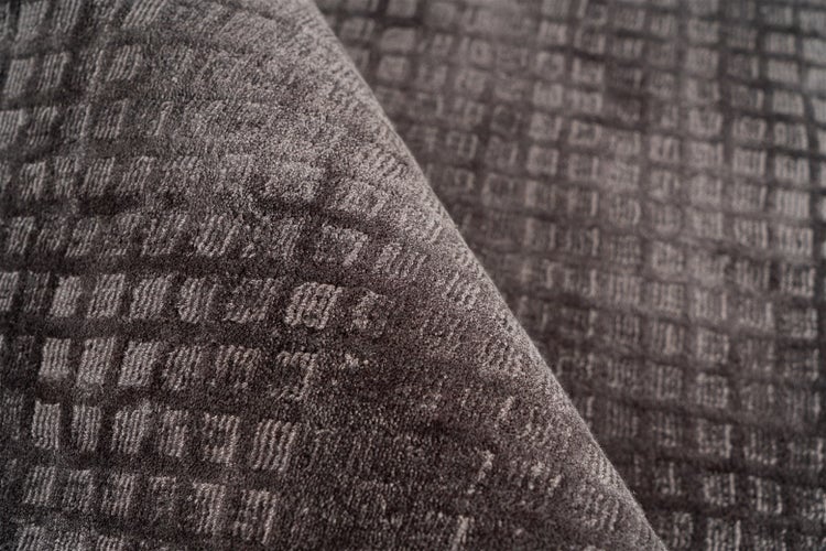 Detailaufnahme eines dunkelgrauen Teppichs mit geometrischem Karomuster und strukturierter Oberfläche.