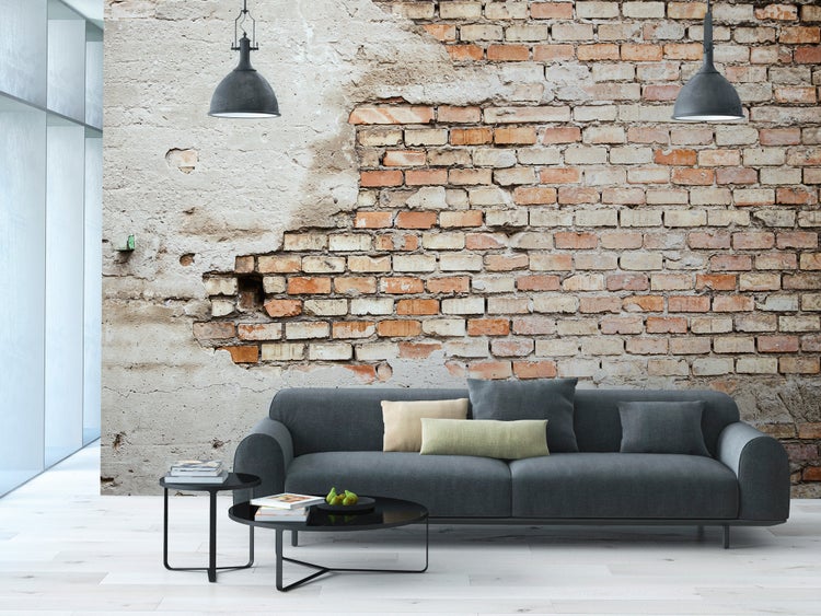 Fototapete in Steinoptik mit Ziegelsteinen und Putz im Wohnzimmer mit grauem Sofa, schwarzen Beistelltischen und Industrieleuchten.