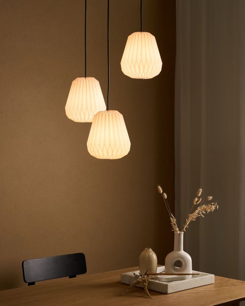 Drei Pendelleuchten mit plissierten Lampenschirmen über einem Holztisch mit Dekoration.